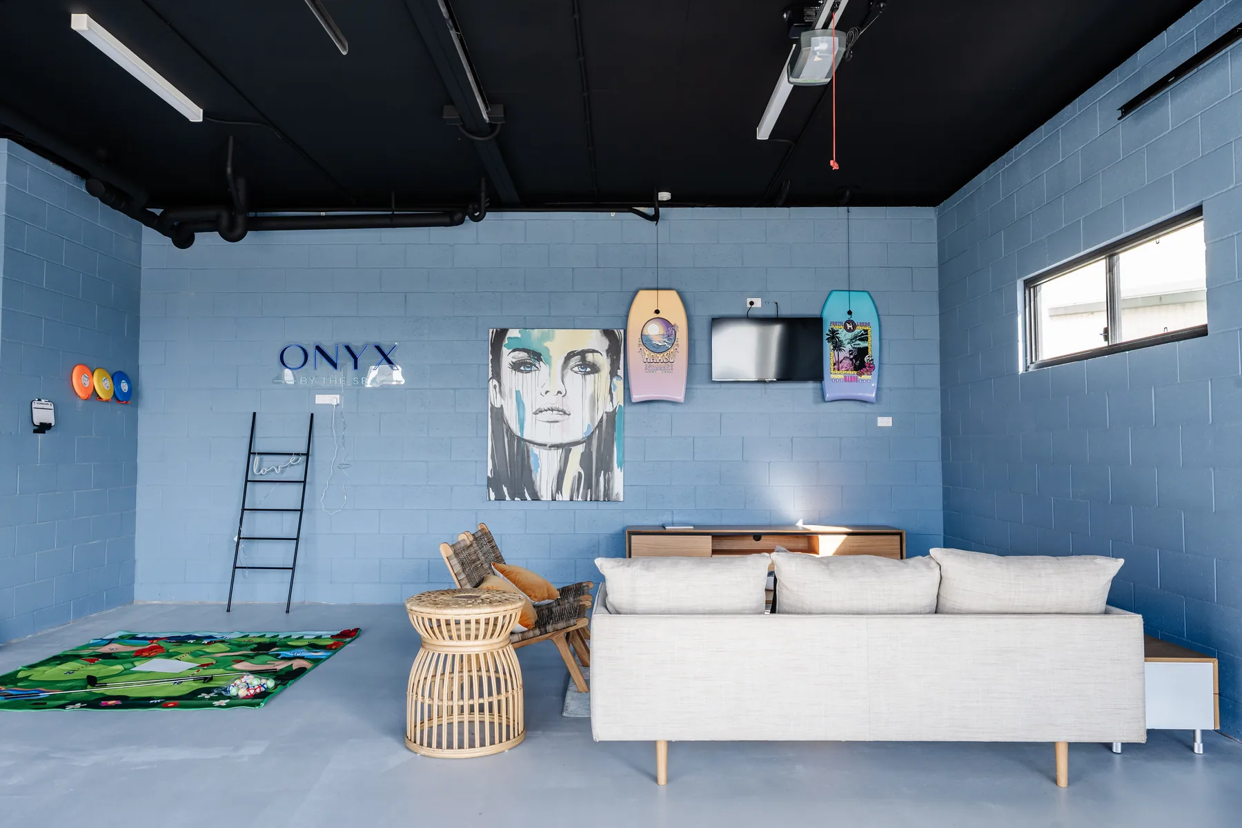 Downstairs garage lounge with blue brick, surfboards and neon
